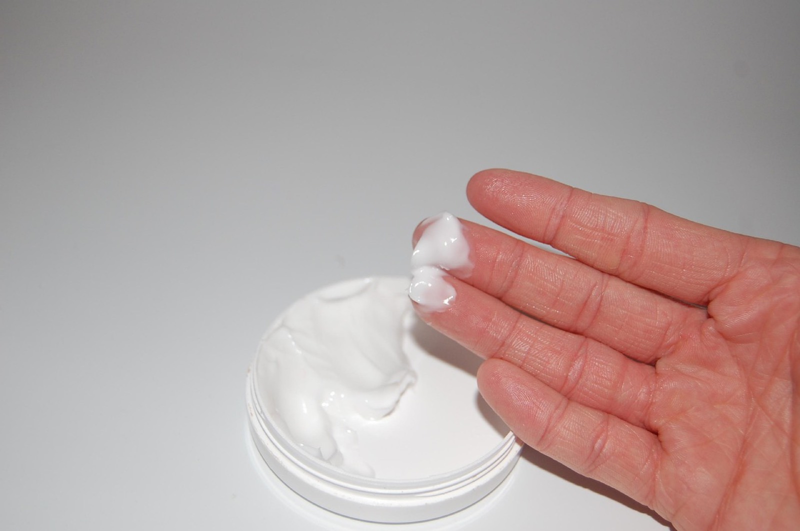 Main tenant un pot de crème hydratante ouvert, soin pour peau mixte à grasse