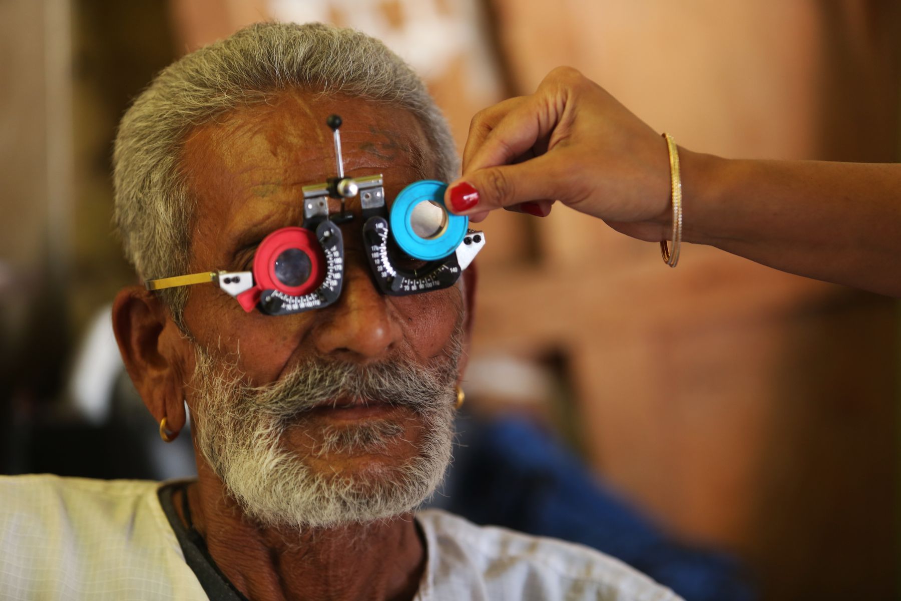 homme âgé à la barbe blanche passant un examen de vue avec une monture d'essai et des verres interchangeables